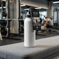 Smartphone with a fitness app displayed on a water bottle in a gym setting